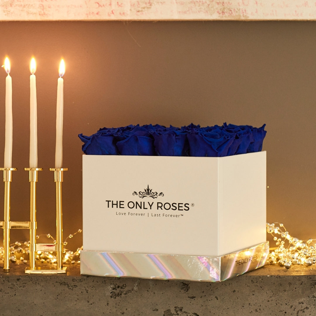 Royal blue roses sit on top of a fireplace beside candle